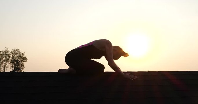 Silhouette of young athlete woman posing on the roof over sunset sky background in summer evening - video in slow motion