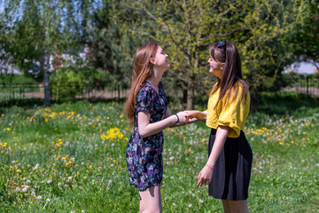 Fototapeta premium Young girls have fun time in the park. The sisters communicate and share secrets. Happy sisters are enjoying a warm spring day