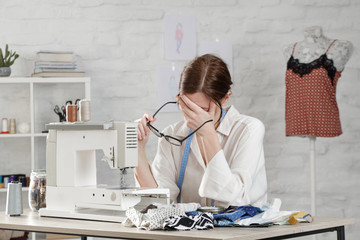 Sleepy, frustrated, exhausted seamstress with headache on her work desk. Small business or...