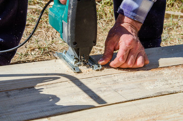 worker sawing boards with a jigsaw at a construction site