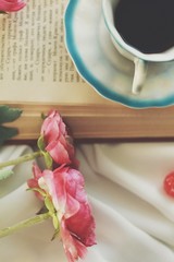 Layout of artificial flowers, a book and a cup with a coffee on a white tablecloth