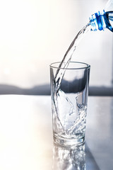 against the background of the window is a glass with clear water from a bottle against the light