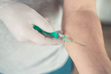 hand in medical gloves with a syringe on a light background