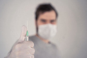 man in a medical mask with a syringe in his hands on a light background