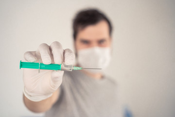 man in a medical mask with a syringe in his hands on a light background