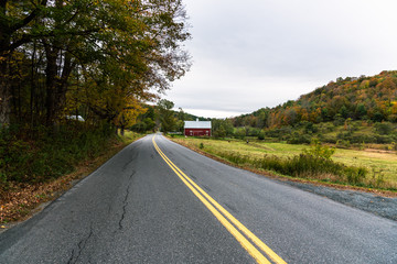 Empty straight road in the countryside on a cloudy autumn day. A red barn is visible on the right side of the road.