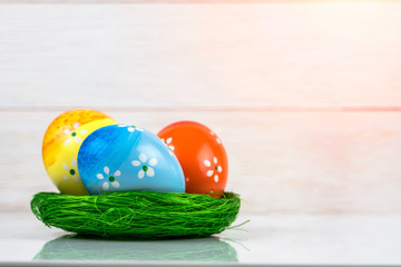 Colourfoul Easter eggs in a green nest and wooden background. Copy space.