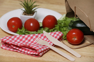 ingredients for cooking. Fresh vegetables on a wooden table. Tomato and salad. Ecology products. Recycle paper bag. Wooden recycle fork and knife