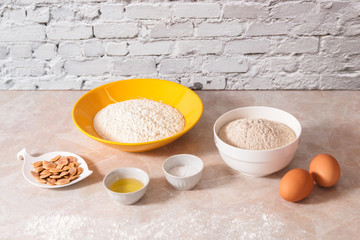 baking ingredients, flour, salt, eggs and oil in white and yellow bowls on marble countertop in bright homey kitchen