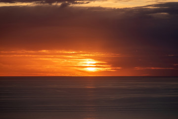 Fototapeta na wymiar Aerial view of distorted sunset sun disk behind layered clouds over ocean horizon