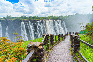 Walking way with view to the dramatic clouds and waterfall at Victoria Falls on the Zambezi River,...
