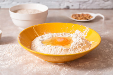 baking ingredients, flour, salt, eggs and oil in white and yellow bowls on marble countertop in bright homey kitchen