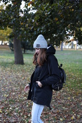 Model in a black coat and grey hat with a backpack. A woman in the fall in a new York city Park