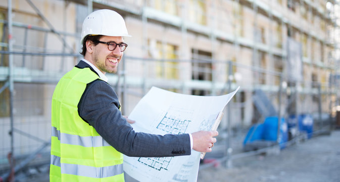 Freudig l&auml;chelnder Architekt auf der Baustelle mit Baupl&auml;nen 