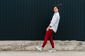 Young female in red leggings and white shirt leaning back hair in the air on black wall background