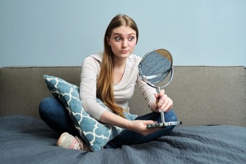 Beautiful young woman with make-up mirror sitting at home in bed