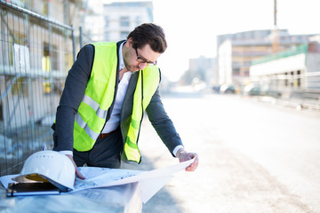 Mann im Anzug mit Helm und Weste auf einer Baustelle