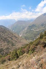 Fototapeta premium Beautiful mountain valley with flowing river in Himalayas in the day. Kongde Ri mountain in the background. Mountainside is covered by forest. Beautiful landscape. Theme of travel in Nepal.
