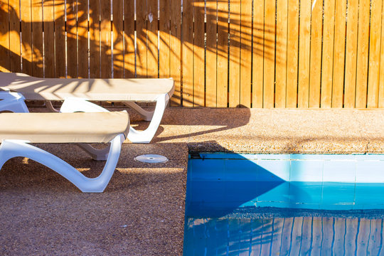 deck chairs near swimming pool site rustic relaxation space on villa back yard sunny lighting shadow from palm on background wooden deck wall object