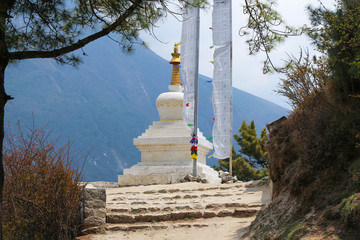 View of typical white stone tibetan buddhist stupa in Himalayas next to waving prayer flags. Clouds...