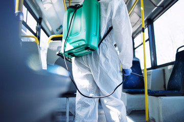 Disinfecting public transportation. An unrecognizable person in white chemical protection suit sanitizing public bus vehicle to stop spreading highly contagious virus. Stop coronavirus or COVID-19.