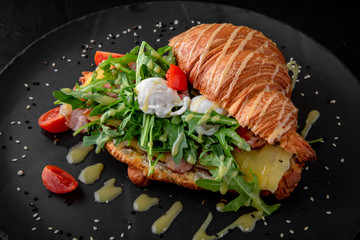 Delicious nutritious sandwich. Croissant with ham, egg, cheese and avocado and arugula. Perfect breakfast.