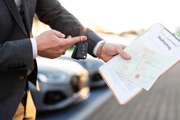 Autokauf, Verkäufer hält Zulassung Papiere und Schlüssel vor einer Reihe an Neuwagen