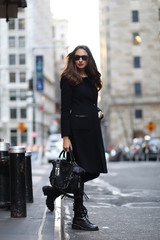 A woman in total black is walking down in New York street. Black coat, bag, jeans, boots, sunglasses