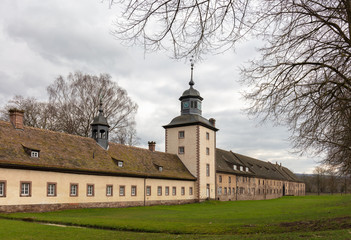 Fototapeta premium The Corvey Castle in eastern North Rhine-Westphalia near the town of Höxter. You can see the western outside with a tower. It is a cloudy winter day, the trees have no leaves.