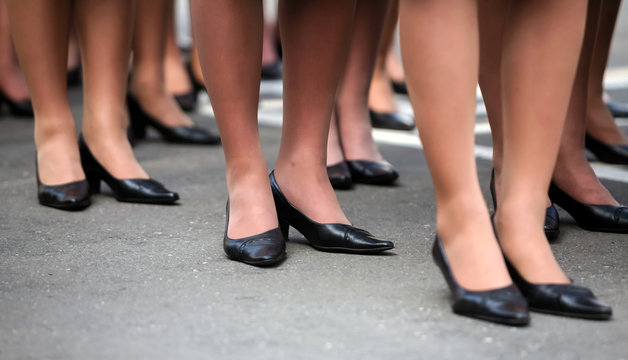 Women's legs in identical black shoes stand in formation.