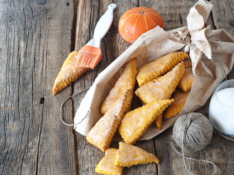 Glazed homemade scones sandwich pumpkin cookies, with tassel for glaze, in paper home packaging, on a wooden ancient background.View from above.