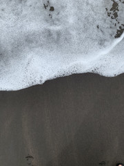 Obraz premium Abstrakt: Schwarzer Sand mit weißer Welle