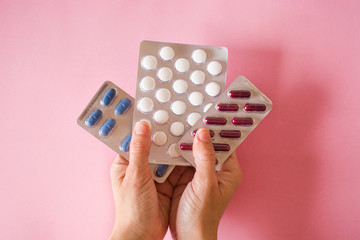 Female hand holding medical pills on pink background