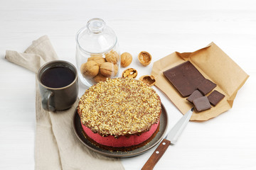 Homemade raspberry cheesecake sprinkled with walnuts crumbs and cup of tea on white wooden table