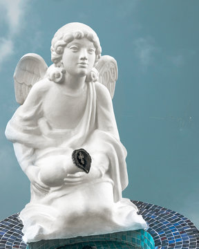 White statue of an angel on his knees with a jug in his hands and an Orthodox cross isolated against a blue sky. Sculpture in Sochi at the Cathedral of the Archangel Michael