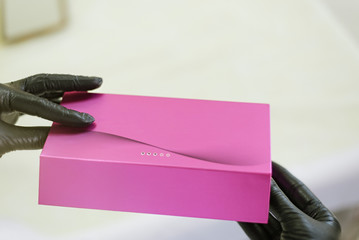 A beautician in black latex gloves holds a closed box with ampoules of filler injection  for smoothing wrinkles