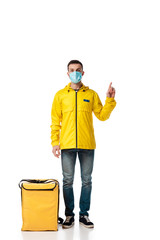 delivery man in medical mask standing near bag with order and pointing with finger on white