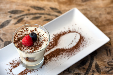 Classic tiramisu dessert in a glass and cup of coffee. Traditional Italian dessert from mascarpone cheese and biscuit in a glass on a vintage table.