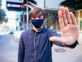 Fototapeta na wymiar Young guy in a blue jacket and mask. Hand raised no