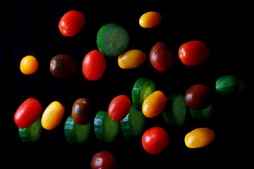 multicolored cherry tomatoes with sliced cucumbers in water drops on a dark background