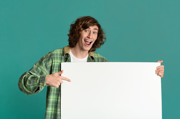 Excited teenage guy pointing at banner with empty space for your design, turquoise background