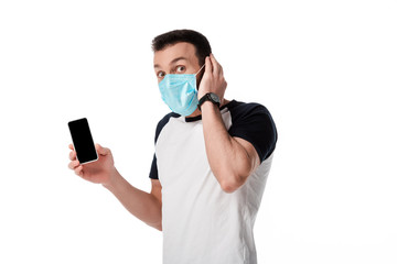 shocked man in medical mask holding smartphone with blank screen isolated on white