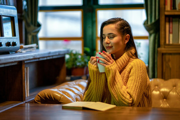 The beautiful woman reading a book on the sofa in front of the window with a cup of coffee