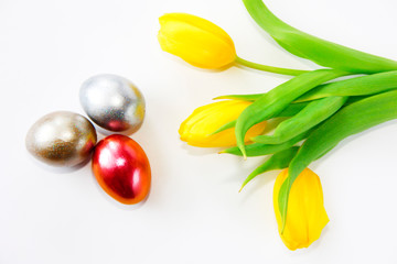 shiny multicolored easter eggs and yellow tulips with green leaves