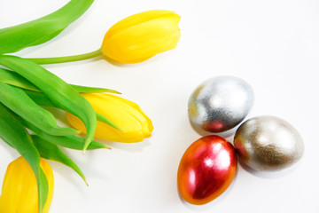 shiny multicolored easter eggs and yellow tulips with green leaves