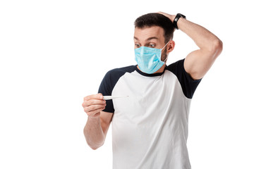 shocked man in medical mask looking at digital thermometer isolated on white