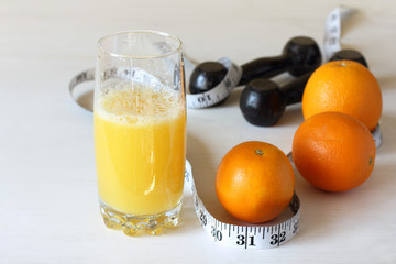 orange juice in a glass on a background of dumbbells and a centimeter. fitness and natural nutrition