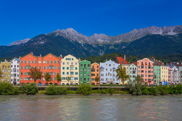 Fototapeta na wymiar Bright and colorful riverside photo of the skyline and buildings of the Austrian Tirol city of Innsbruck, guided by its background alps.