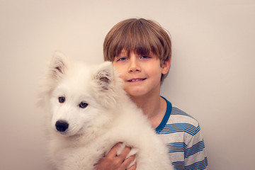 Cute boy holding his puppy samoyed dog posing for camera.