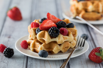 A close up view of a stack of Belgian waffles topped with various berries ready for eating.
